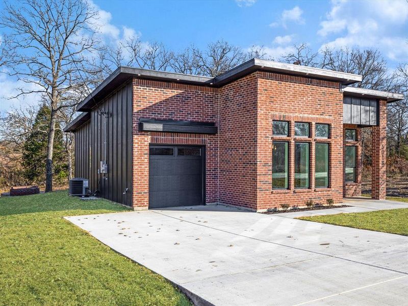 View of side of home with board and batten siding, concrete driveway, a lawn, and brick siding View of side of home with board and batten siding, concrete driveway, a lawn, and brick siding