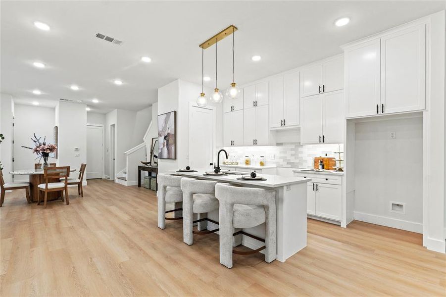 Kitchen with white cabinetry, pendant lighting, tasteful backsplash, a kitchen bar, and a kitchen island with sink Kitchen with white cabinetry, pendant lighting, tasteful backsplash, a kitchen bar, and a kitchen island with sink