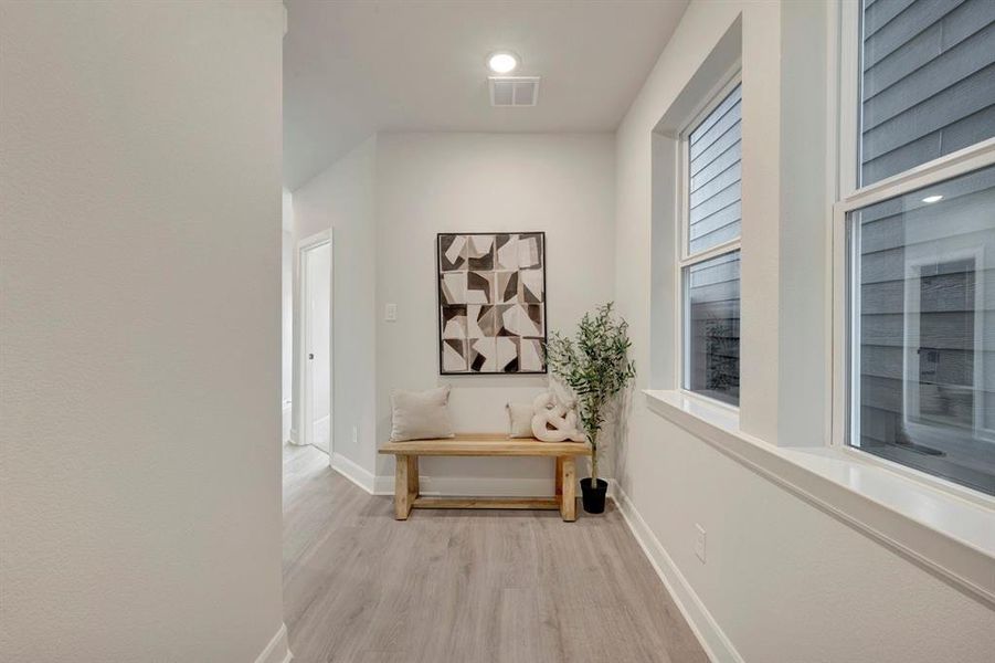 Hallway featuring light wood-finish flooring, white baseboards, and bright white walls