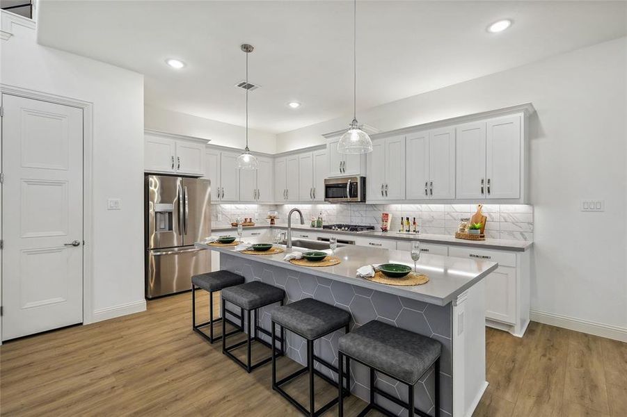 Modern kitchen featuring white shaker cabinetry, stainless steel appliances, a light gray countertop island with hexagonal tile detailing, and wood-finish flooring