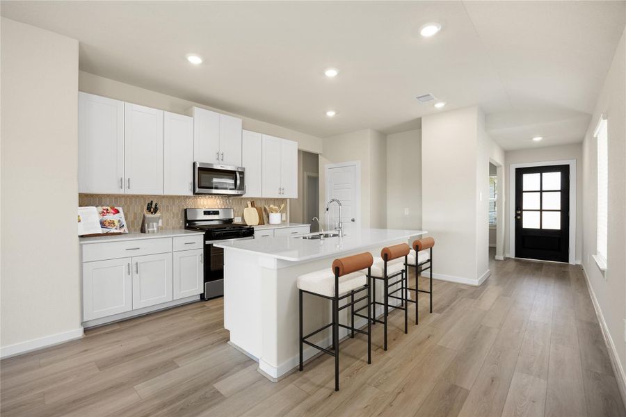 This modern kitchen showcases sleek white cabinetry, stainless steel appliances, quartz countertops, modern tile backsplash and a large island with breakfast bar seating. The open design and neutral palette create a bright, inviting atmosphere ideal for gatherings or quiet mornings at home.