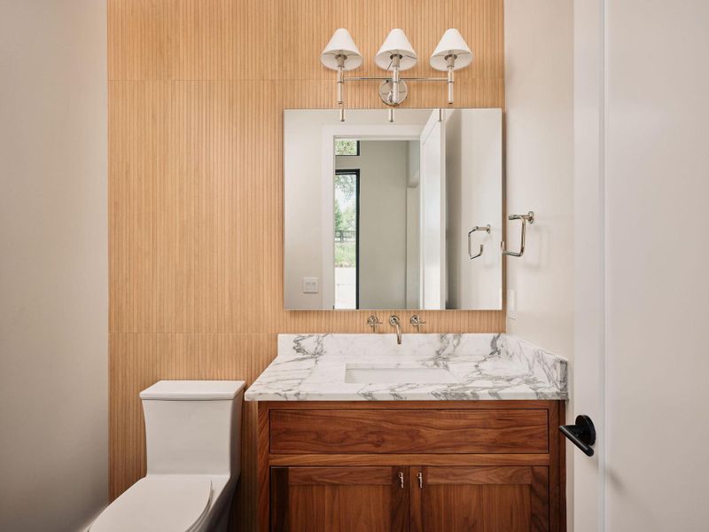 Marble countertops adorn this vanity, complemented by rich wooden cabinetry and a modern toilet. Marble countertops adorn this vanity, complemented by rich wooden cabinetry and a modern toilet.