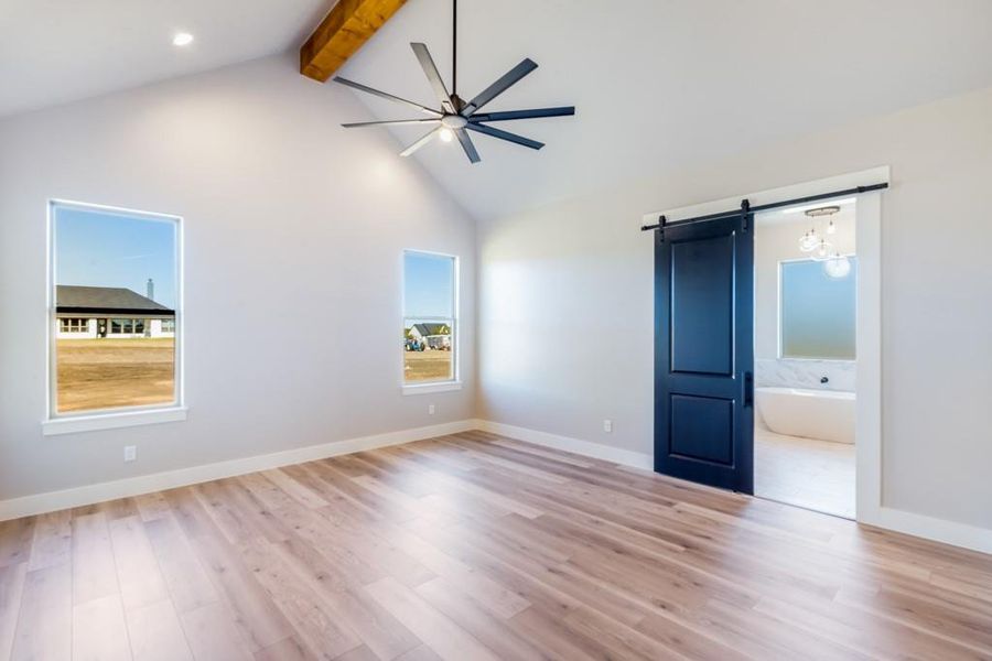 Unfurnished bedroom featuring a barn door, ensuite bathroom, lofted ceiling with beams, and light hardwood / wood-style floors