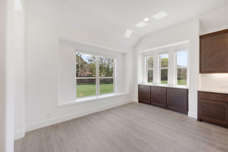 Bright dining area with light wood floors, dark wood built-in cabinets, and large windows overlooking a backyard