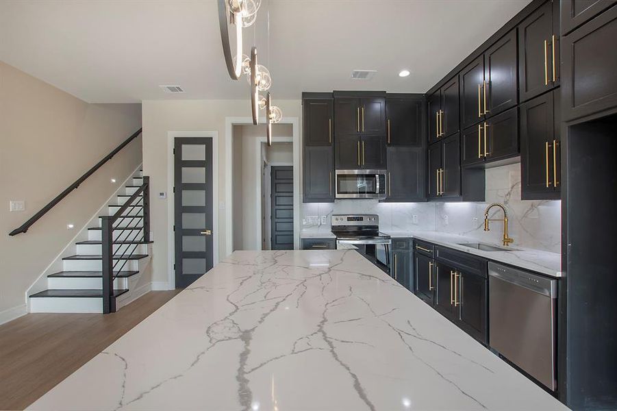 Kitchen featuring pendant lighting, backsplash, dark hardwood / wood-style floors, light stone counters, and stainless steel appliances