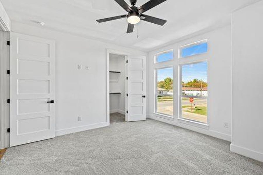 Unfurnished bedroom with ceiling fan, a walk in closet, and light carpet