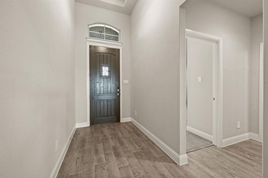 Bright entryway highlighted by a tall ceiling, wood-look tile floors, and natural light flowing through the decorative transom window.