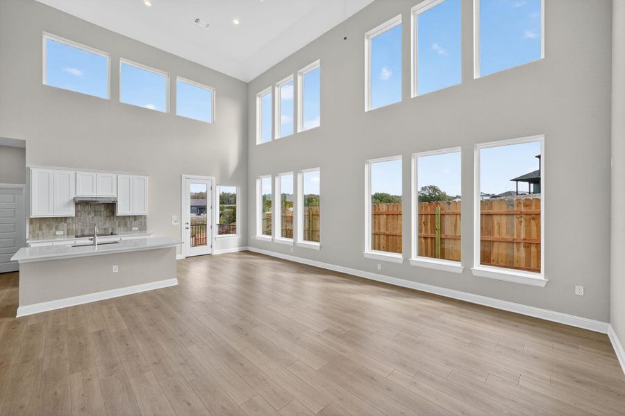 Unfurnished living room with light wood finished floors, a towering ceiling, and recessed lighting Unfurnished living room with light wood finished floors, a towering ceiling, and recessed lighting