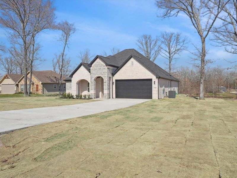 French country style house featuring driveway, an attached garage, a front lawn, stone siding, and brick siding