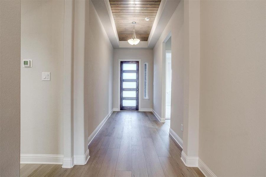 Entryway featuring light wood-type flooring, a raised ceiling, and wood ceiling