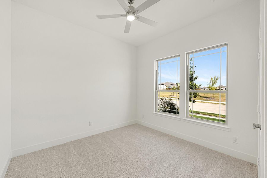 Empty bedroom with white walls, carpet flooring, ceiling fan, and two windows with neighborhood views