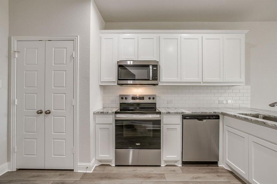 Kitchen featuring stainless steel appliances, white cabinetry, light stone counters, backsplash, and light wood-style floors