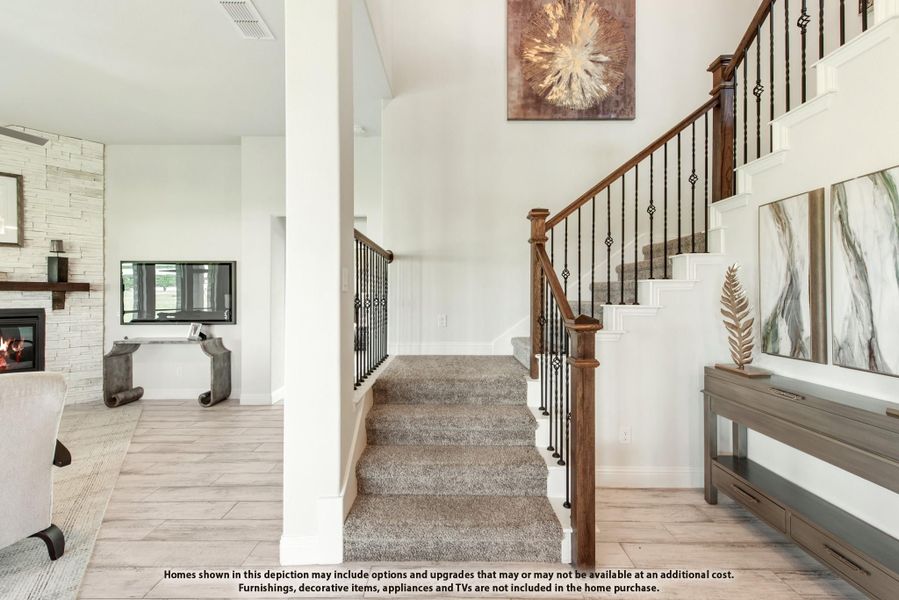 Carpeted staircase with wood and iron railing, open to living room with stone fireplace and tile floors