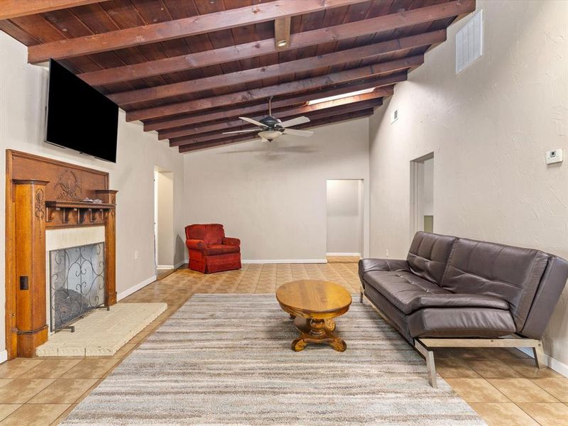 Living area featuring a wooden ceiling with exposed beams, a fireplace with raised hearth, light tile patterned floors, and ceiling fan Living area featuring a wooden ceiling with exposed beams, a fireplace with raised hearth, light tile patterned floors, and ceiling fan