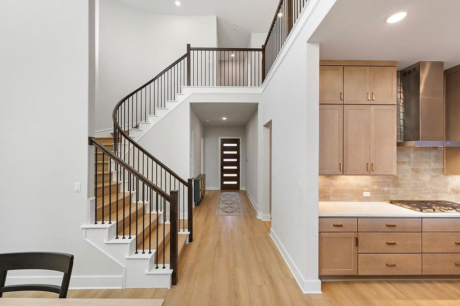 An elegant curved staircase anchors the open foyer, flowing seamlessly into the kitchen area.