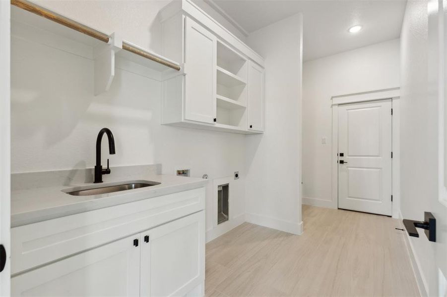 Laundry area with light hardwood / wood-style flooring, washer hookup, cabinets, electric dryer hookup, and sink