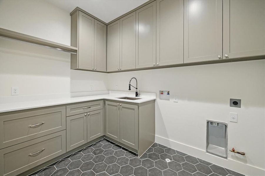 The second-floor laundry room offers functionality and style with custom cabinetry, sleek hardware, and a deep utility sink. A practical layout provides ample countertop space for folding and storage while the hexagonal tile flooring adds a modern touch.