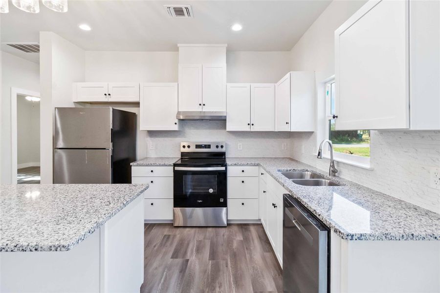 Kitchen featuring appliances with stainless steel finishes, light stone counters, white cabinetry, light wood-style flooring, and recessed lighting