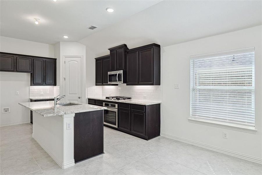 Kitchen featuring appliances with stainless steel finishes, tasteful backsplash, a kitchen island with sink, and sink