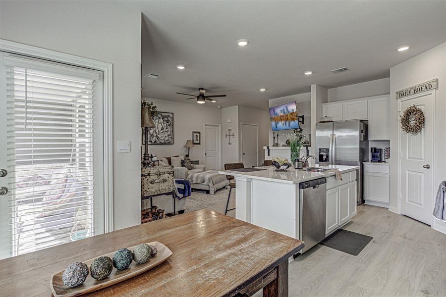 Kitchen with white cabinetry, a center island with sink, a ceiling fan, light wood-style floors, and open floor plan