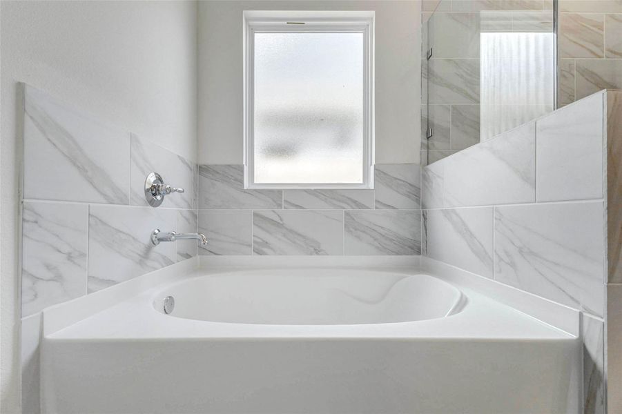 Soaking tub in the primary bathroom surrounded by marble-look tile and a privacy window for soft natural light. This relaxing feature pairs beautifully with the separate shower to create a comfortable owner’s bath retreat.