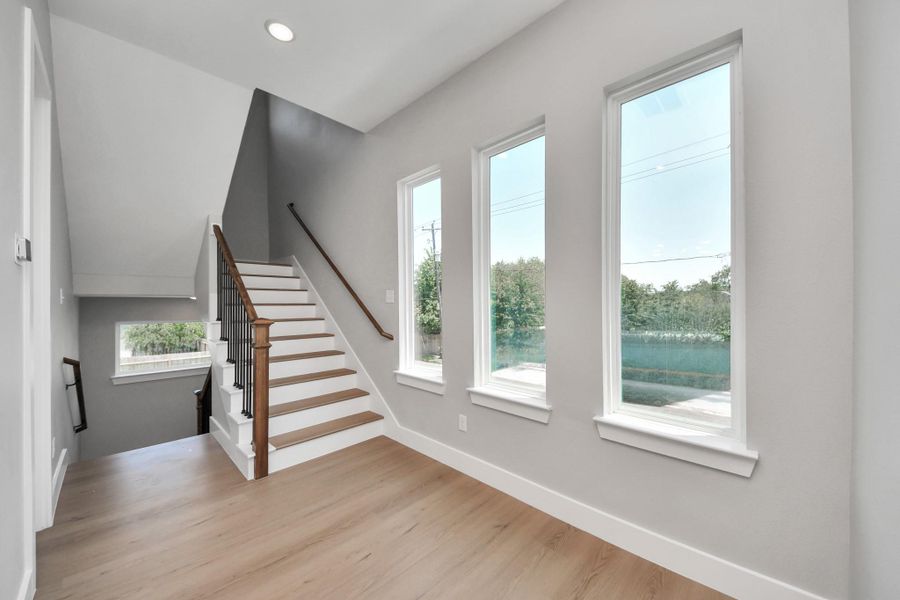Light-filled landing area featuring oversized windows, modern staircase design, & warm contemporary finishes throughout.