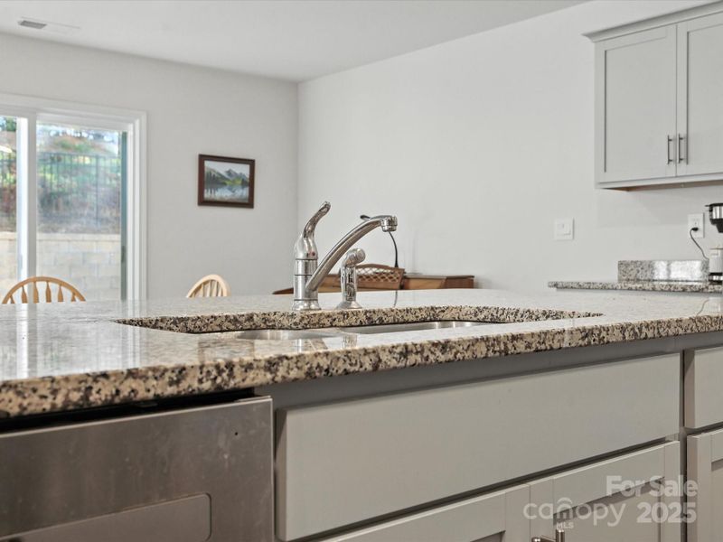 Functional kitchen island features undermount sink with granite countertops and convenient bar seating. Open concept design allows easy interaction between kitchen and living spaces.