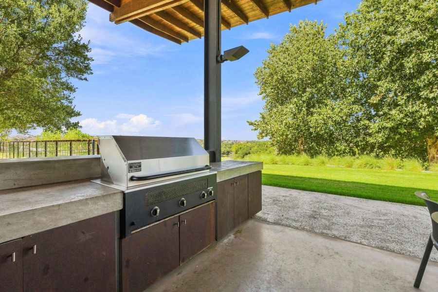 An outdoor kitchen features durable concrete countertops beneath a sheltering wood-beamed pavilion.