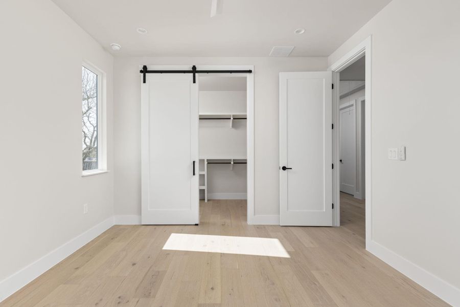 Unfurnished bedroom featuring a barn door, a spacious closet, wood finished floors, and baseboards