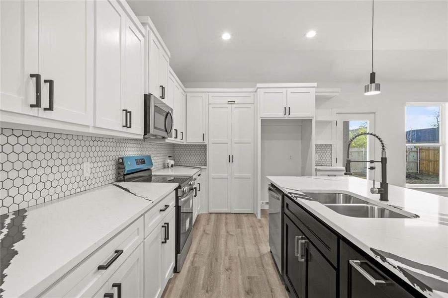 Kitchen with pendant lighting, white cabinets, sink, appliances with stainless steel finishes, and tasteful backsplash