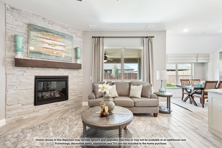 Living room with stacked stone fireplace, wood mantel, gray sofa, and hardwood floors open to dining area Living room with stacked stone fireplace, wood mantel, gray sofa, and hardwood floors open to dining area