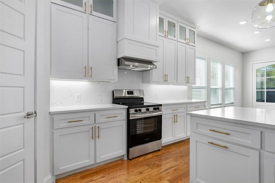 Kitchen featuring white cabinets, decorative backsplash, light hardwood / wood-style flooring, and stainless steel range oven