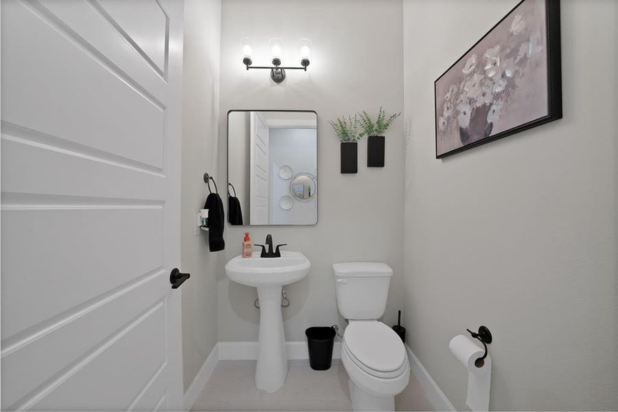 Pedestal sink with matte black faucet, framed mirror, and three-light vanity fixture Pedestal sink with matte black faucet, framed mirror, and three-light vanity fixture