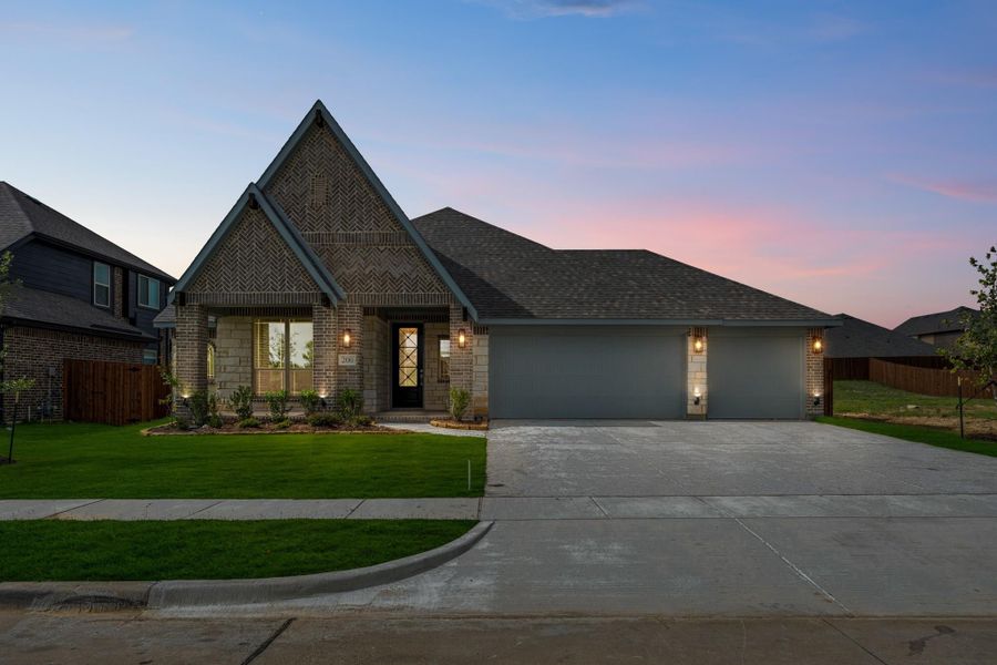 Single-story brick home with steep gabled roofline, two-car garage, and landscaped front yard at dusk