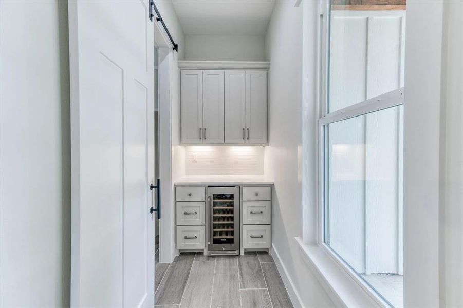 Bar with tasteful backsplash, white cabinetry, a barn door, light hardwood / wood-style floors, and beverage cooler