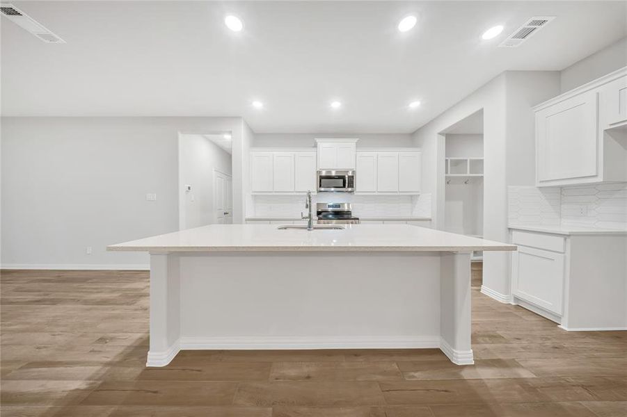 Kitchen featuring appliances with stainless steel finishes, a center island with sink, light wood-style floors, tasteful backsplash, and recessed lighting Kitchen featuring appliances with stainless steel finishes, a center island with sink, light wood-style floors, tasteful backsplash, and recessed lighting