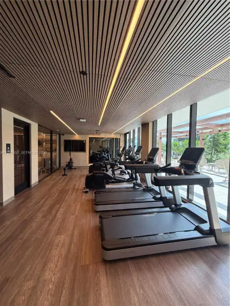 Slatted wood-finish ceiling with integrated linear LED lighting, wood-finish flooring, floor-to-ceiling glass windows, and glass-paneled entry door