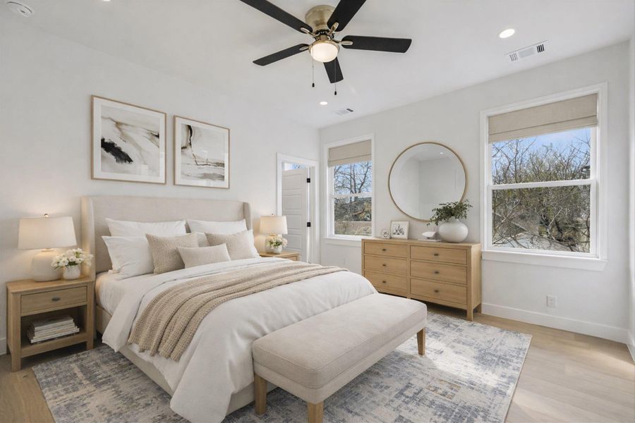 Staged photo. Your peaceful escape awaits. The primary suite features large windows that pull in the afternoon sun and beautiful wide-plank flooring that continues throughout the upper level.