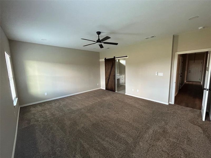 Unfurnished bedroom with a barn door, ceiling fan, dark carpet, and ensuite bath