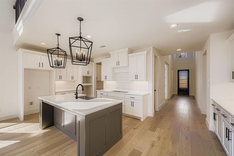 Kitchen featuring white cabinets, a kitchen island with sink, decorative light fixtures, backsplash, and light wood-style flooring