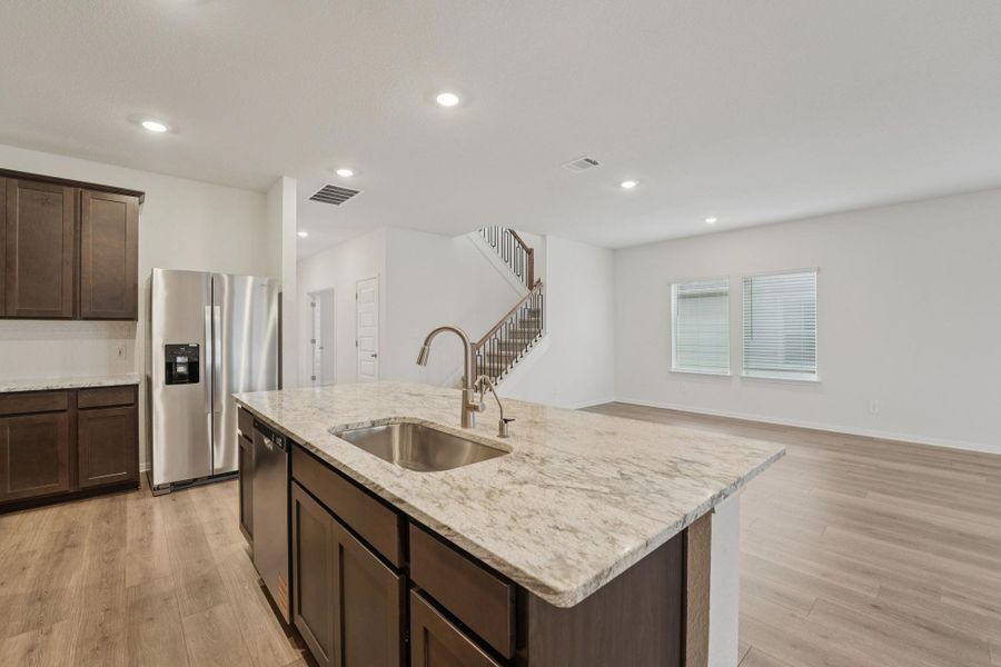 Kitchen featuring dark brown cabinets, stainless steel appliances, light wood-style flooring, light stone countertops, and recessed lighting