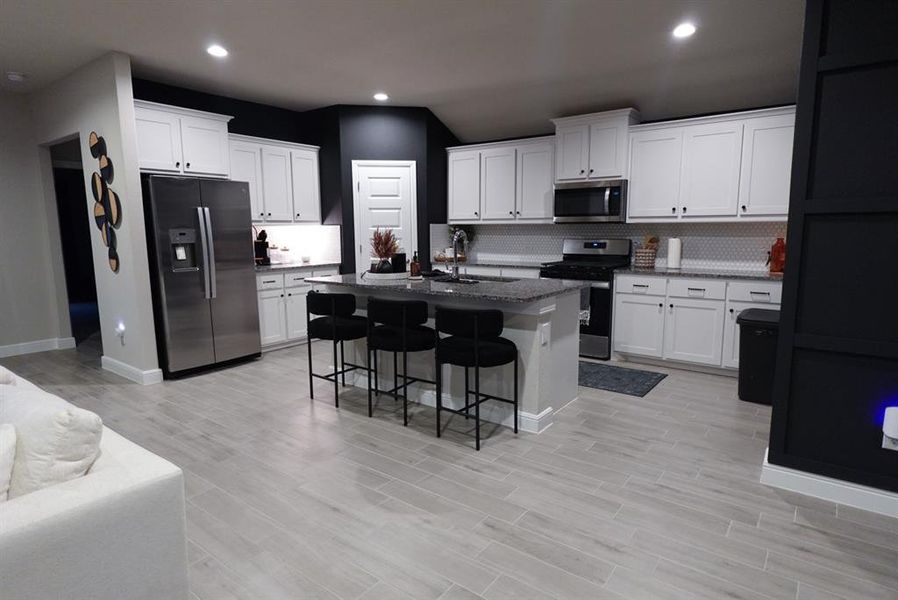 Modern kitchen featuring an expansive island with seating, white shaker cabinetry, stainless steel appliances