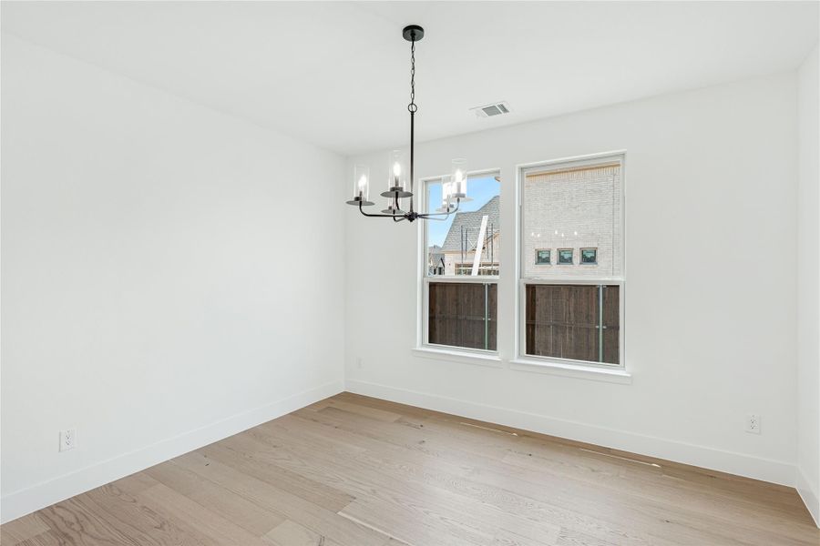 Empty dining room with light hardwood floors, white walls, black chandelier, and two windows Empty dining room with light hardwood floors, white walls, black chandelier, and two windows
