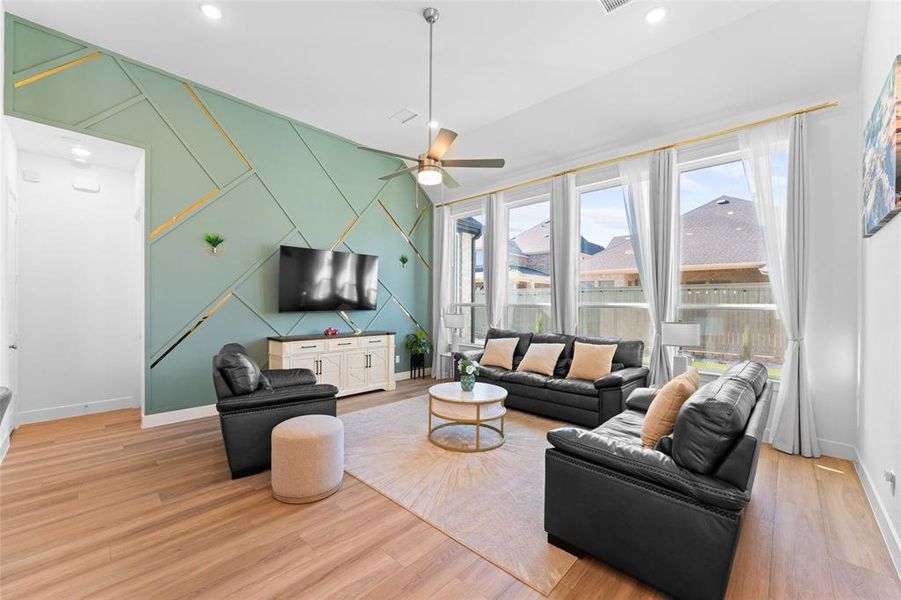 Spacious living room featuring hardwood floors, a decorative accent wall, and large windows providing natural light