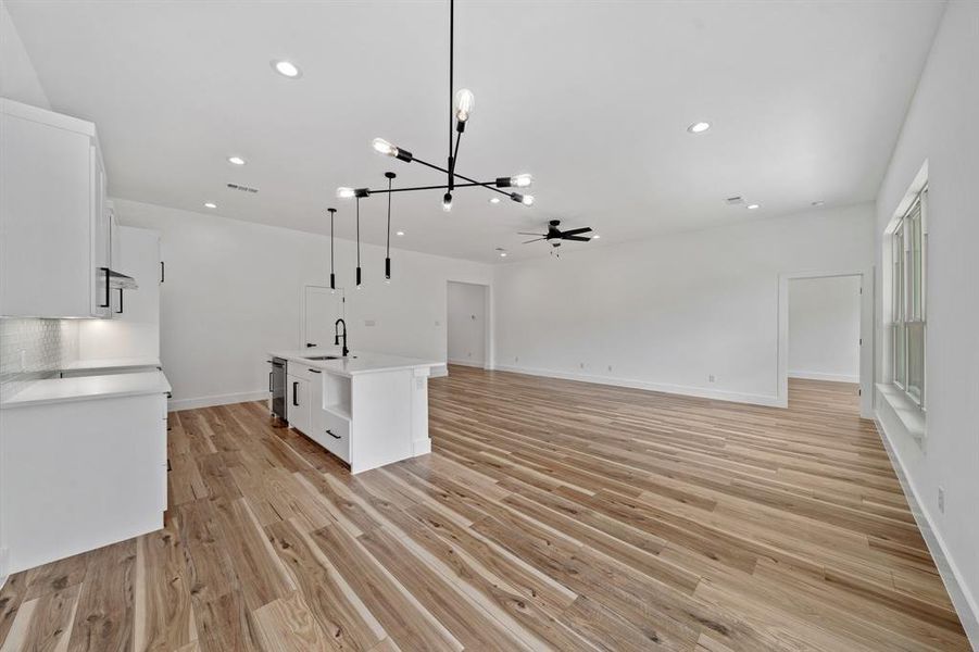 Kitchen featuring an island with sink, light hardwood / wood-style flooring, pendant lighting, white cabinets, and ceiling fan with notable chandelier