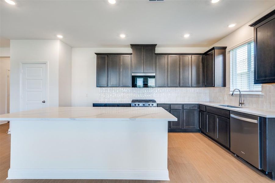 Kitchen featuring decorative backsplash, a center island, light wood finished floors, stainless steel appliances, and light stone counters