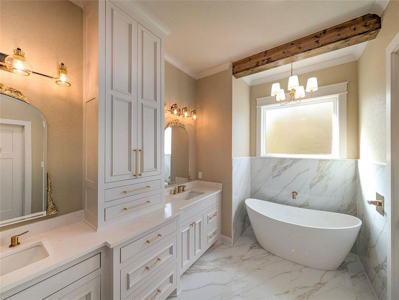 Bathroom with light marble finish flooring, tile walls, a wainscoted wall, double vanity, and a freestanding bath