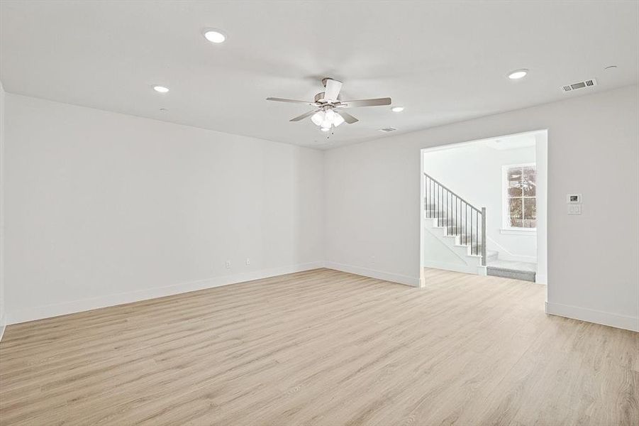 Empty room featuring visible vents, light wood-style flooring, a ceiling fan, stairway, and baseboards