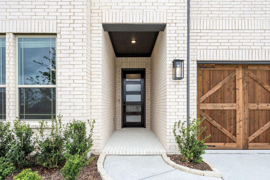 Home entrance with black glass front door, white brick exterior, covered entry, and wood garage door nearby