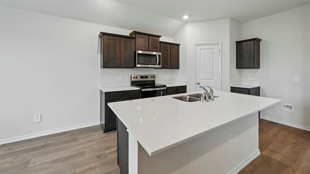 Kitchen featuring stainless steel appliances, a center island with sink, light stone countertops, light wood-style floors, and recessed lighting